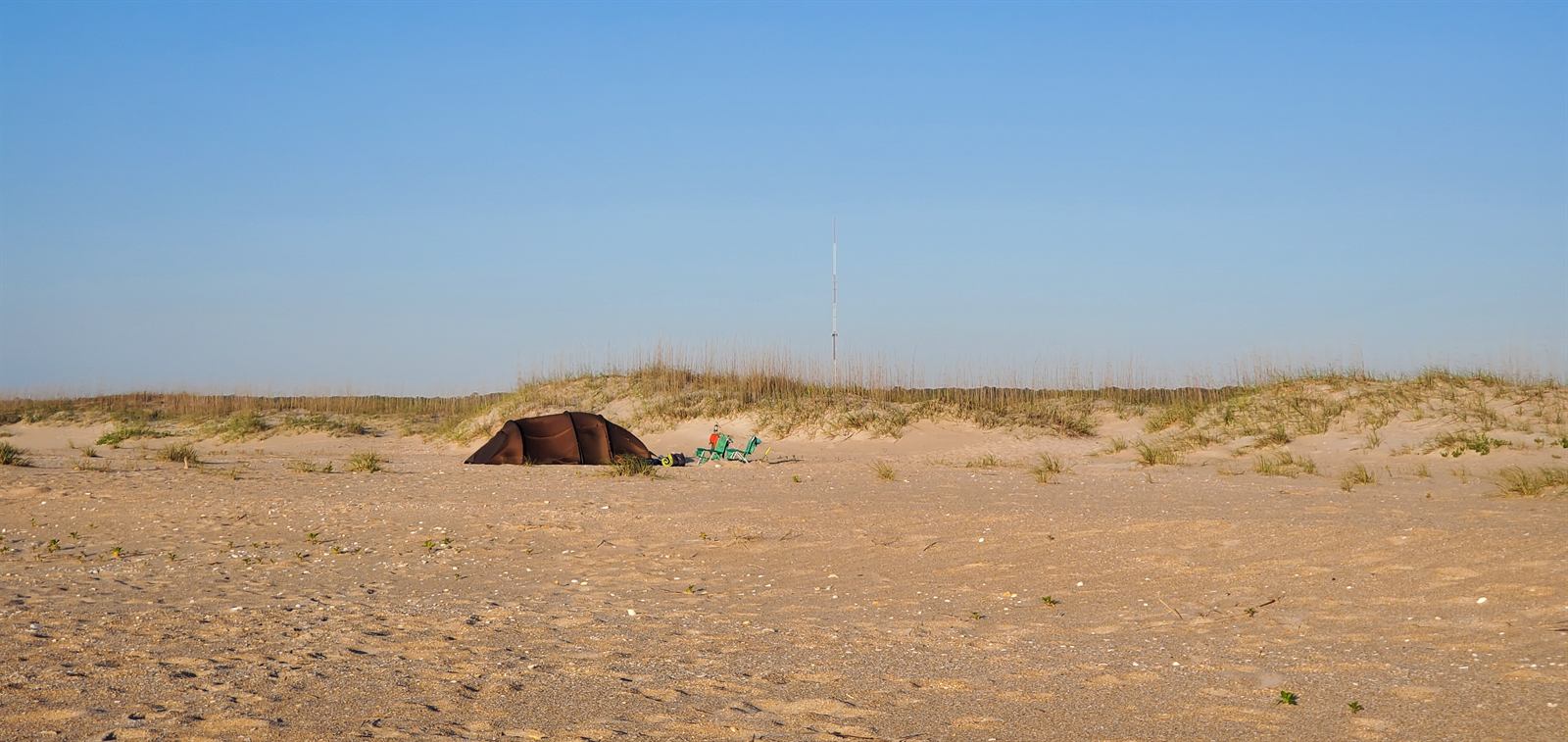 Camp set up on open sand below the dunes, chairs out, early morning