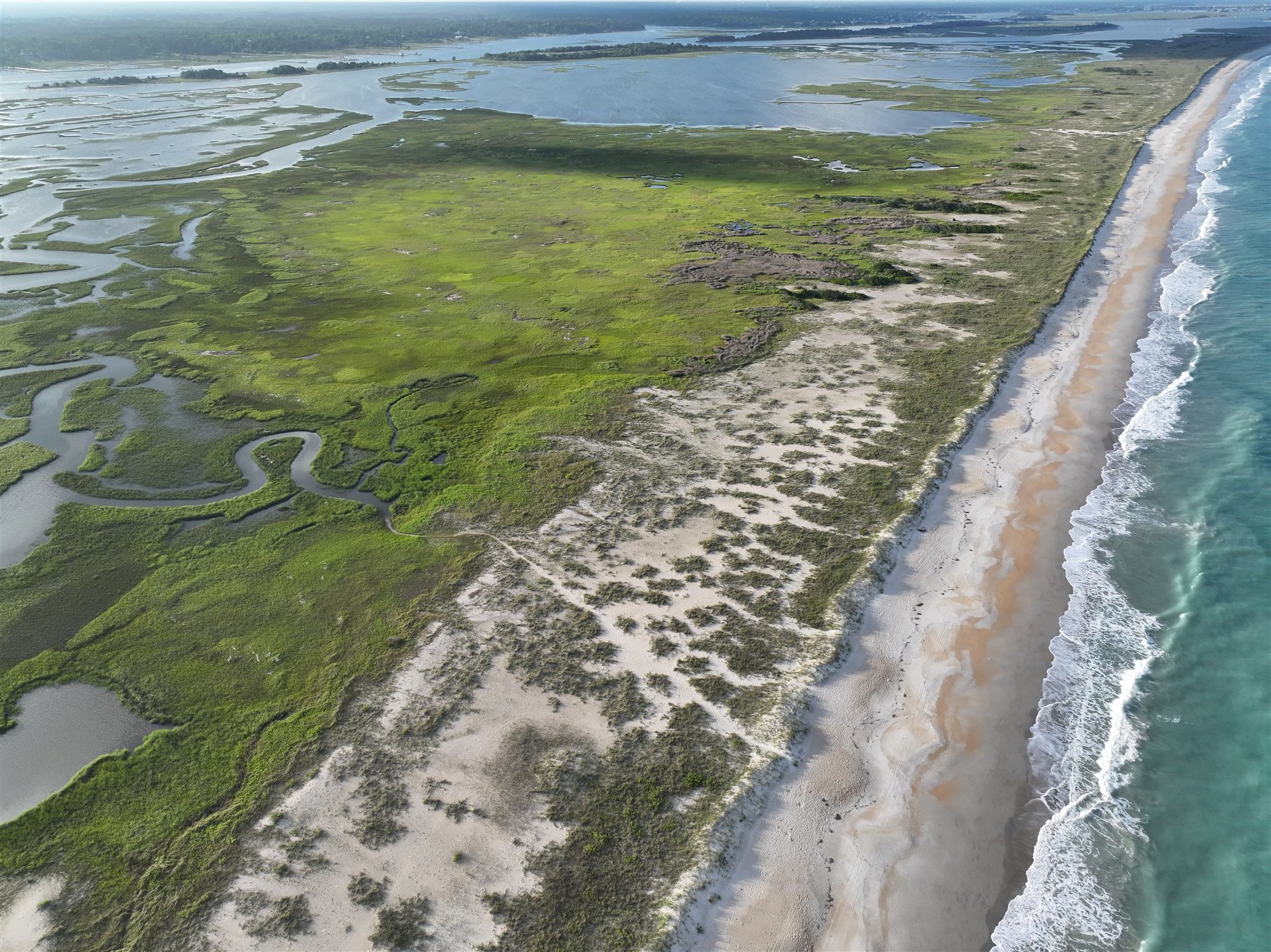 Aerial view across Masonboro Island: ocean surf, open beach, dunes, salt marsh and the sound beyond